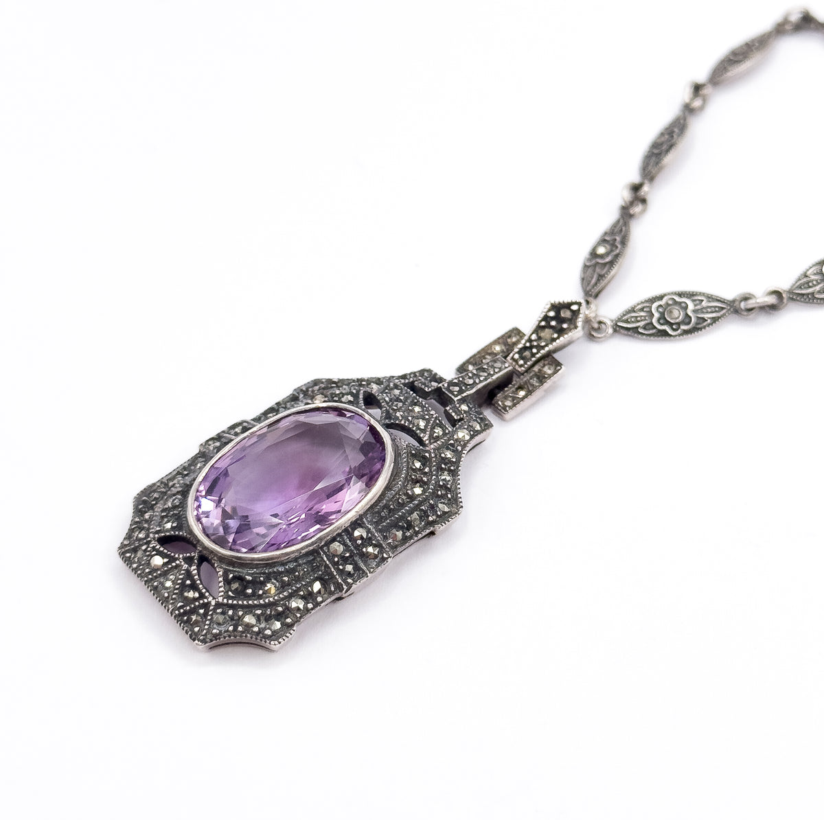 Diagonal full view of the necklace laid out on white, the amethyst pendant at lower left and the chain sweeping to the upper right corner, showing how pendant, stepped links and chain connect.
