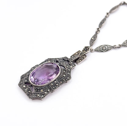 Diagonal full view of the necklace laid out on white, the amethyst pendant at lower left and the chain sweeping to the upper right corner, showing how pendant, stepped links and chain connect.