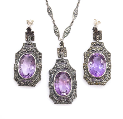 The complete set laid flat on white, the pendant with its chain in the centre flanked by both drop earrings with posts and backs visible, showing all three oval amethysts together.