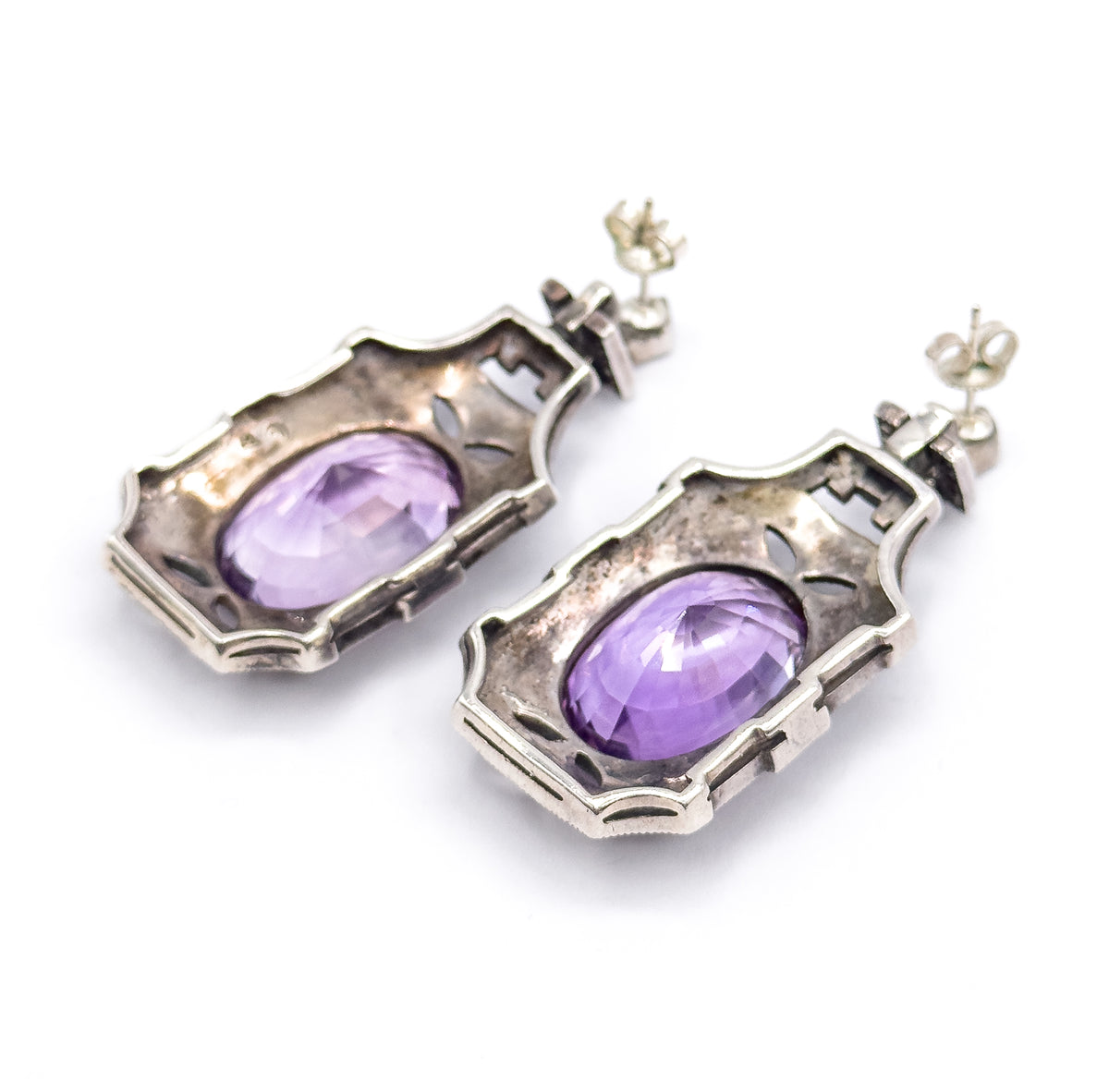 Low angled view of the backs, the shaped silver plates and their pierced cut-outs rising away from the camera with the amethyst pavilions domed through each open bezel and the butterflies behind.
