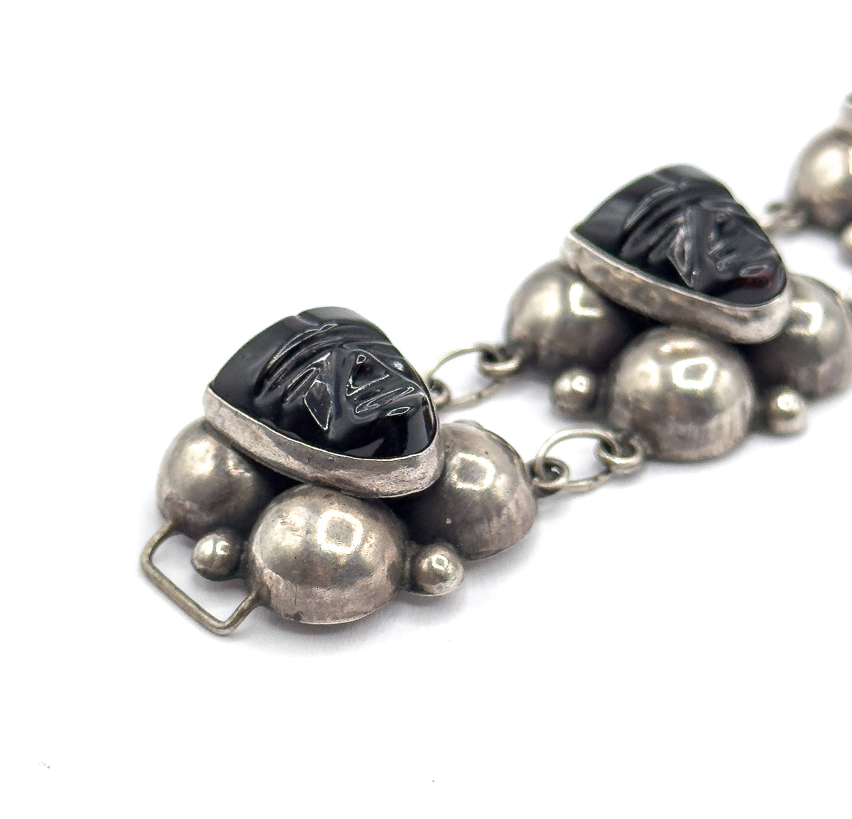 Steep diagonal view from the clasp end, the squared wire clasp frame jutting from the lower station's silver domes while two carved onyx faces in their bezels angle away up the chain.