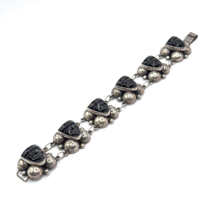 The whole bracelet laid out flat and stretched corner to corner, all six carved onyx face stations with their silver domes in a line between the hook at one end and the flat tab at the other.