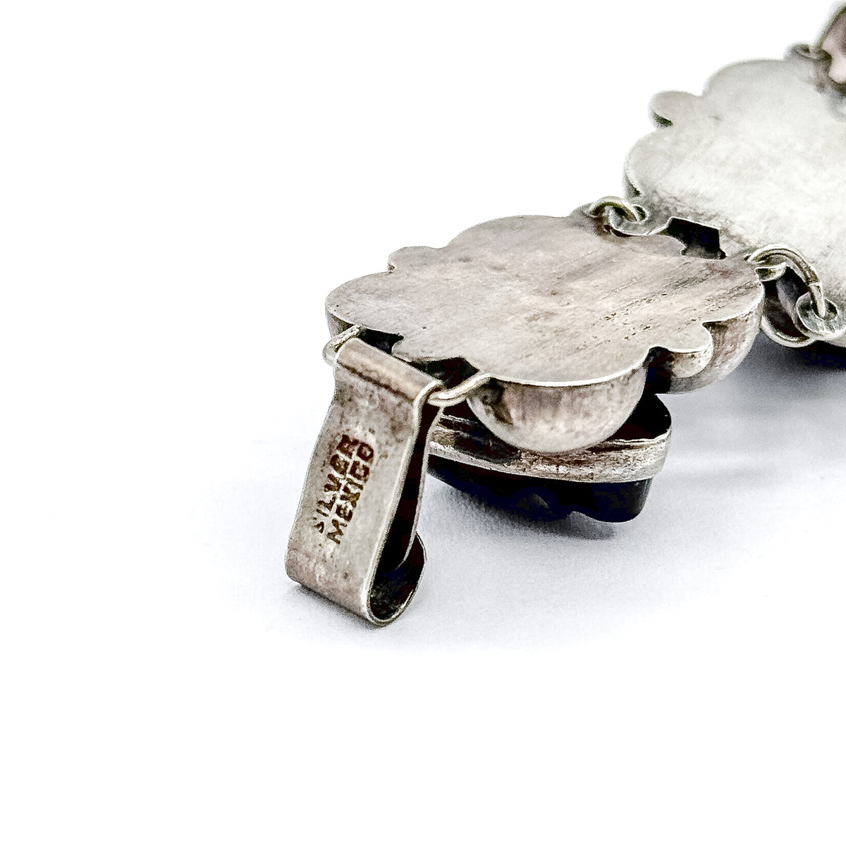 Macro of the folded clasp tongue, stamped "silver mexico", lying beside the smooth scalloped back of an end station and its oval connecting link.