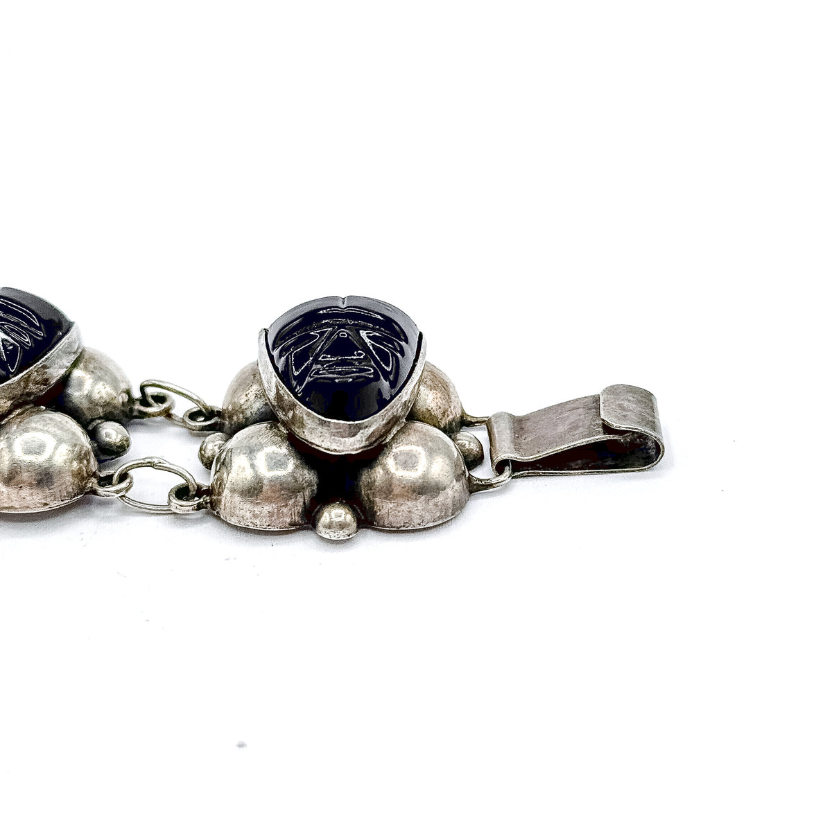 Angled view of the end station with its bezel-set carved onyx face tipped towards the camera, the flat folded clasp blade extending to one side beyond the silver domes.