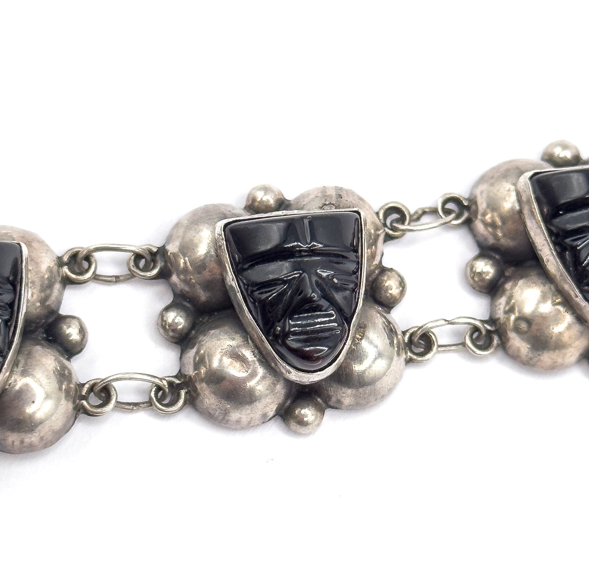 Tight macro centred on one carved onyx face, its bezel and surrounding silver domes filling the frame, with the oval links and neighbouring stations trailing off to either side.