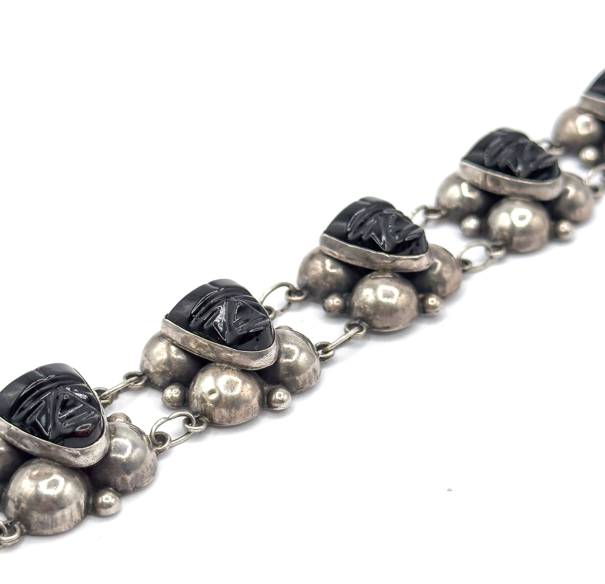 Low, raking view along the length of the bracelet, four carved onyx face stations receding diagonally into the distance with their domed silver clusters and paired oval links in a row.