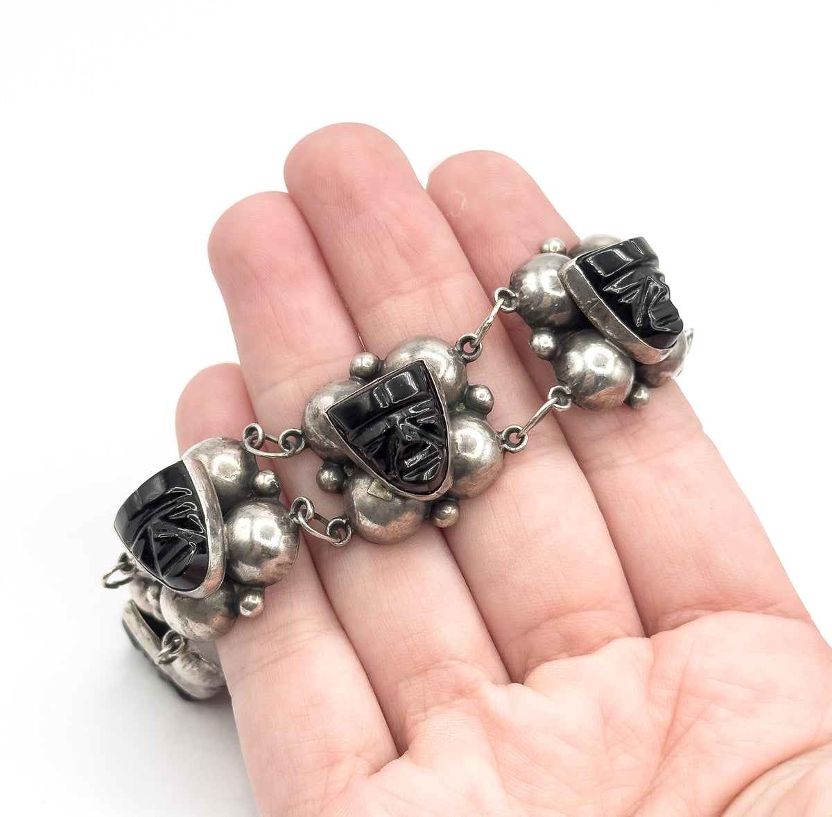 Mid-century sterling silver bracelet with carved black onyx faces bezel-set in puffy domed stations, draped across an open palm to show its size.