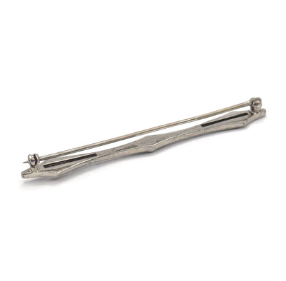 Art Deco filigree bar brooch in sterling silver, shown from the back at a diagonal on a white background, with the long pin stem, hinge and catch visible along the slim tapered bar.