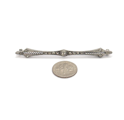 Front view laid flat beside a dime for scale, the slim filigree bar set with small paste gems and a larger central stone in a round bezel.