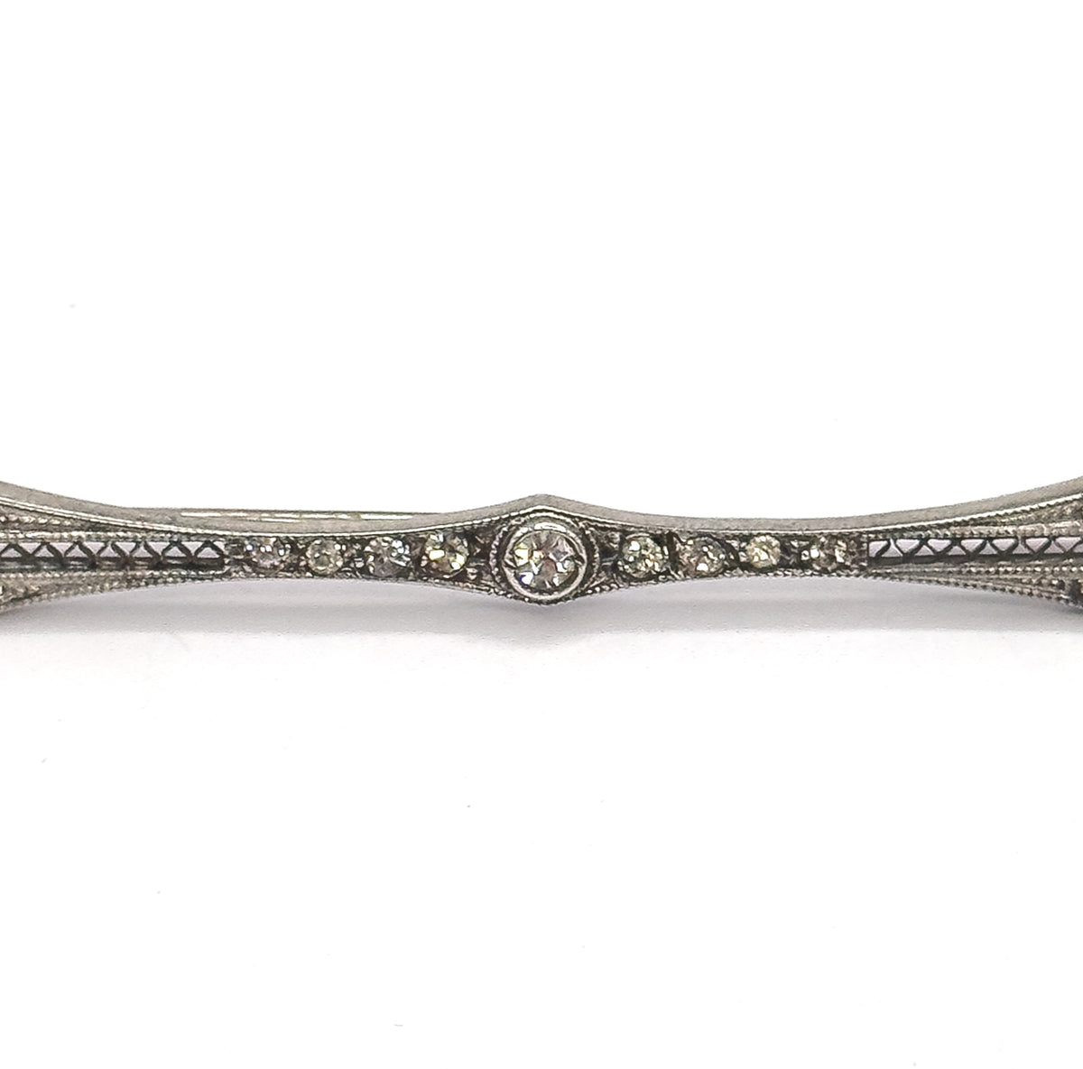 Tight close-up of the brooch's midsection, the central paste gem in its round bezel flanked by graduated rows of small pastes above triangular filigree piercing, the bar running off both edges.