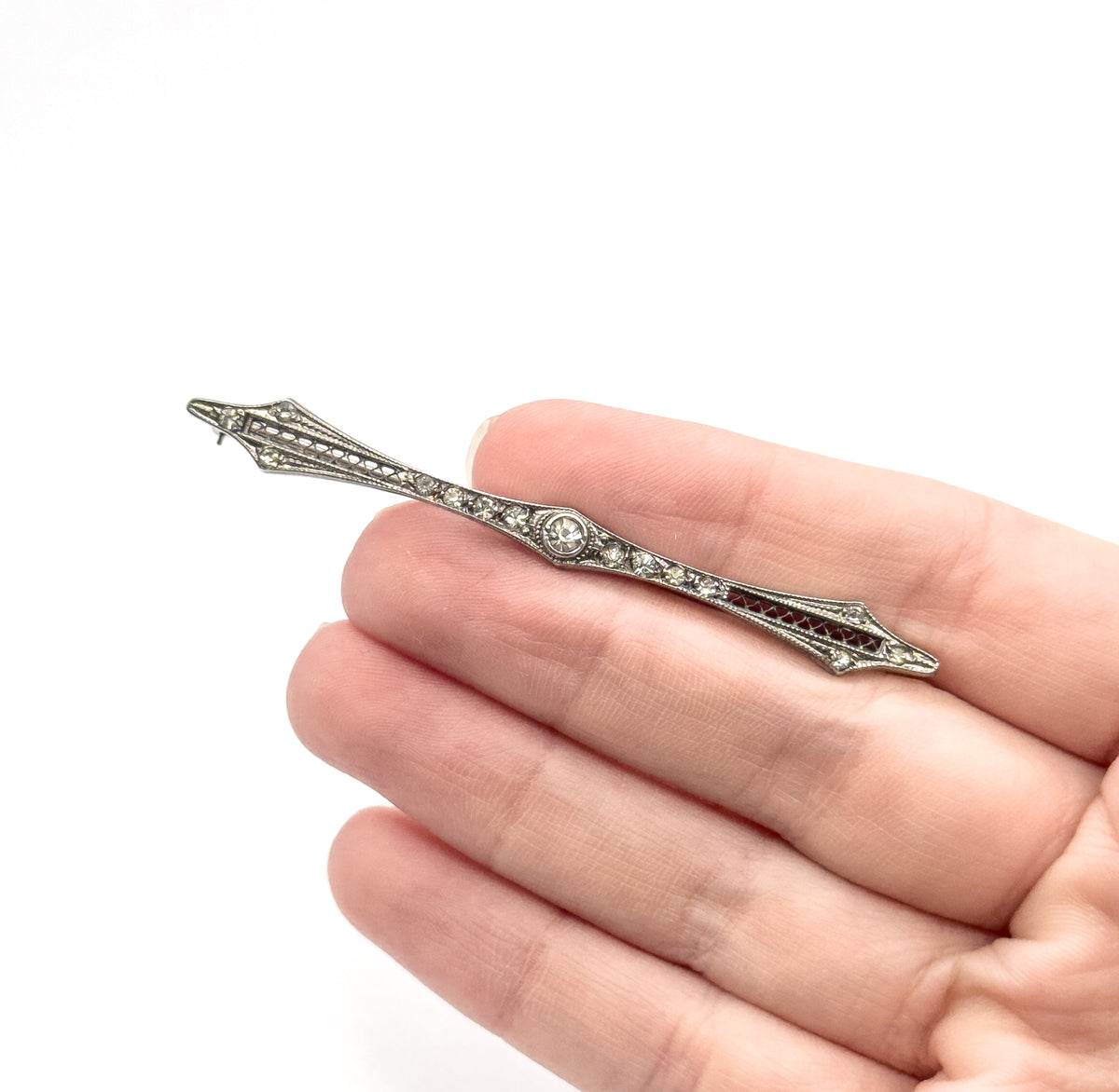 The slim bar brooch laid diagonally across four open fingers, giving a clear sense of its small scale, with the pin stem just visible beyond the upper point.