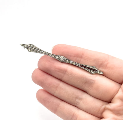 The slim bar brooch laid diagonally across four open fingers, giving a clear sense of its small scale, with the pin stem just visible beyond the upper point.