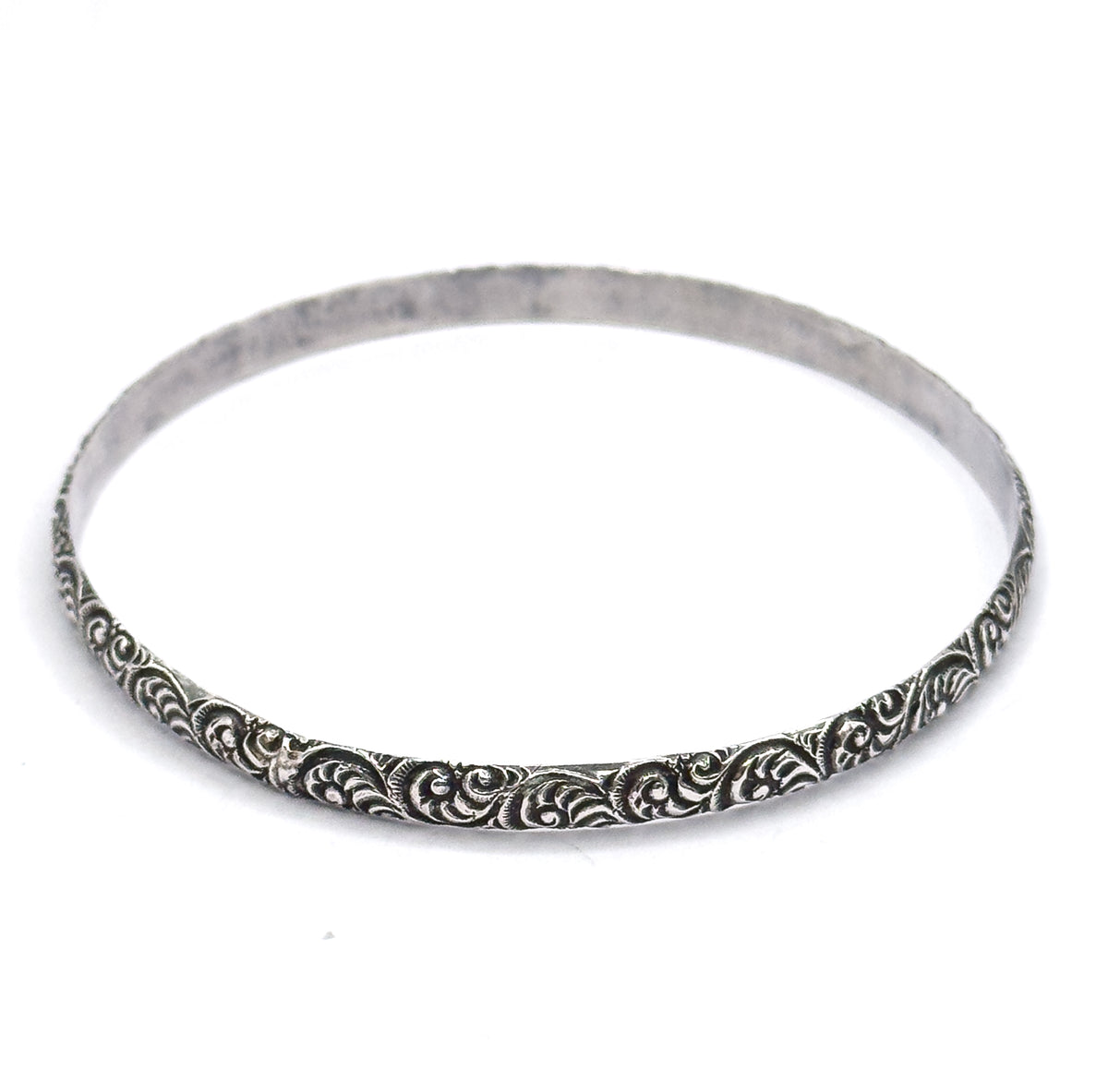 Tilted at an angle on white, the oval band rises away from the viewer so the plain smooth inner surface shows while the raised swirls catch the light along the near outer edge.