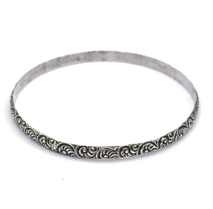 Tilted at an angle on white, the oval band rises away from the viewer so the plain smooth inner surface shows while the raised swirls catch the light along the near outer edge.