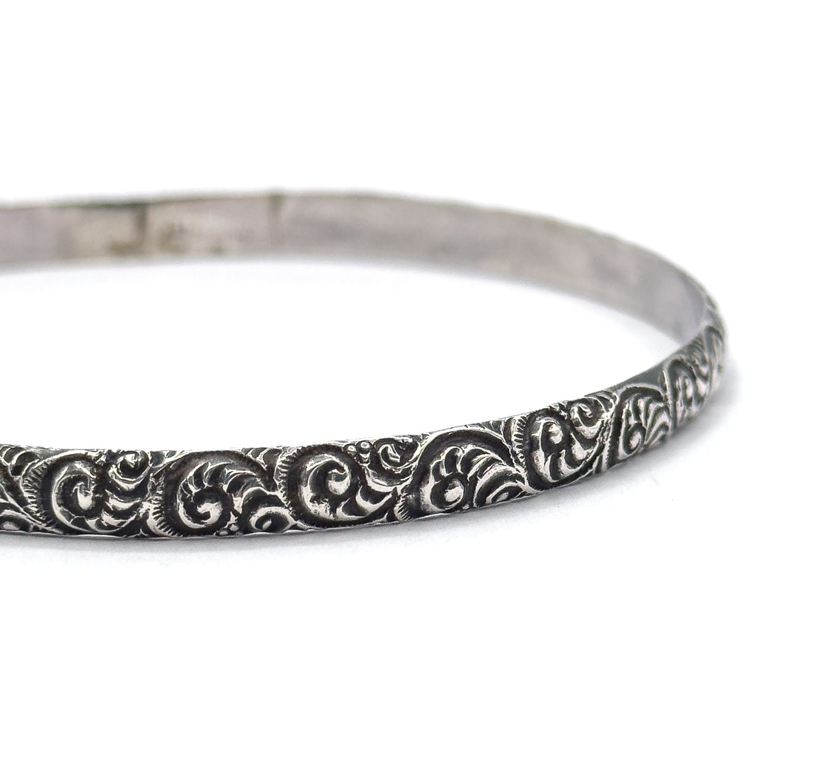 Close crop on one side of the band, filling the frame so each raised swirl and the darkened recesses between them can be seen in detail against white.