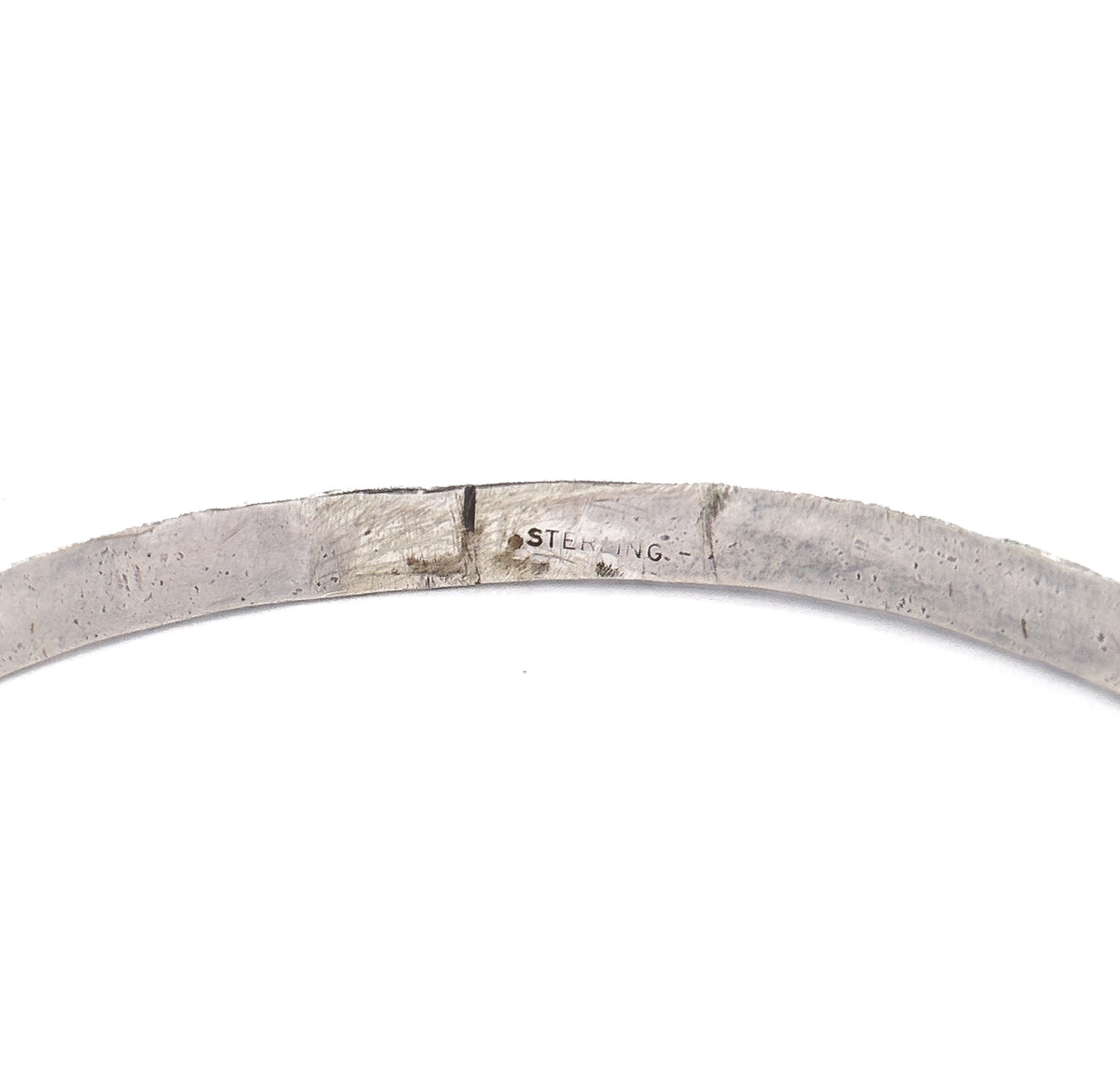 Macro view of the smooth inner surface of the band, where the word "sterling" is stamped in small letters beside a seam in the silver.