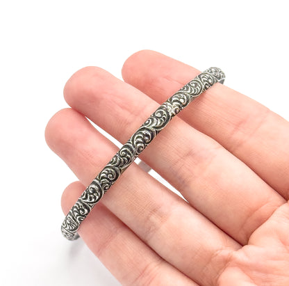 Mid-Century sterling silver cuff bracelet, shown resting across the fingers of an open hand for scale, its raised swirl pattern with darkened patina running the length of the band.