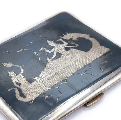 Tighter diagonal crop on the lid's engraving, where a crowned figure kneels raising a leaf-shaped form while a standing figure rides the scaled serpent boat, the clasp just visible at lower right.