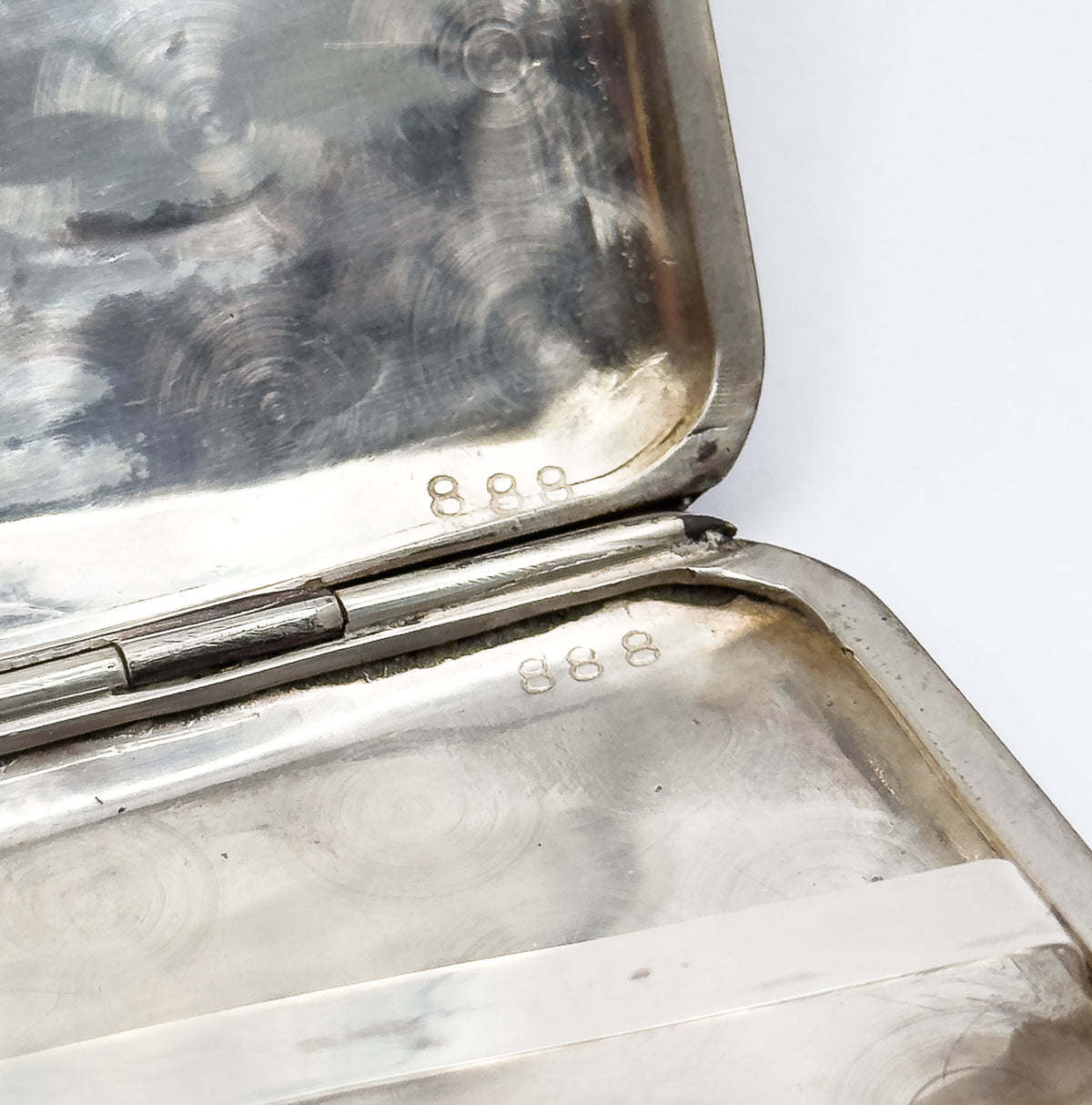 Opened interior corner showing the hinge barrel running between the two halves, each stamped 888 on its polished light-metal rim.