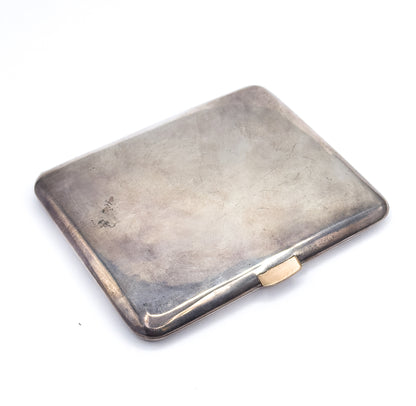 Closed and angled on a white surface, the case rests face up showing a plain smooth rectangular lid with softly rounded corners and a small contrasting clasp thumbpiece on the long edge.