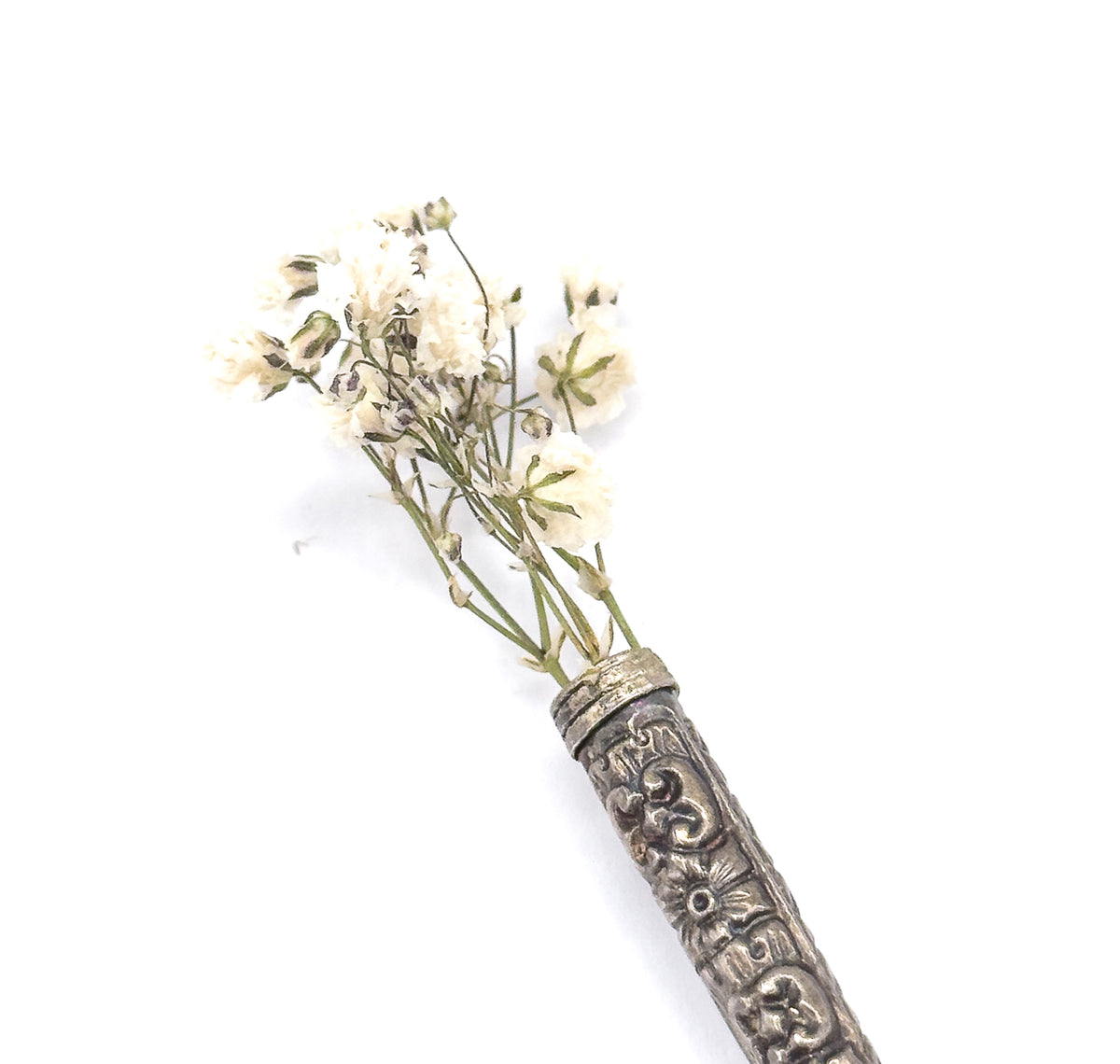 The repoussé sterling silver cone shown upright against white, its scrolled and floral patterning visible, with tiny white dried flowers tucked into the open rim like a posy holder.