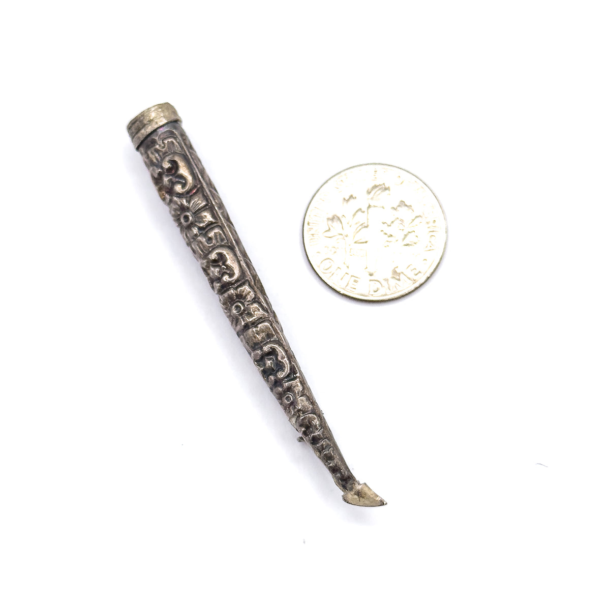 The cone lies beside a dime for scale, showing it to be roughly twice the coin's width in length, with its repoussé patterning and tapering pin stem clear.