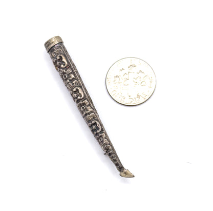 The cone lies beside a dime for scale, showing it to be roughly twice the coin's width in length, with its repoussé patterning and tapering pin stem clear.