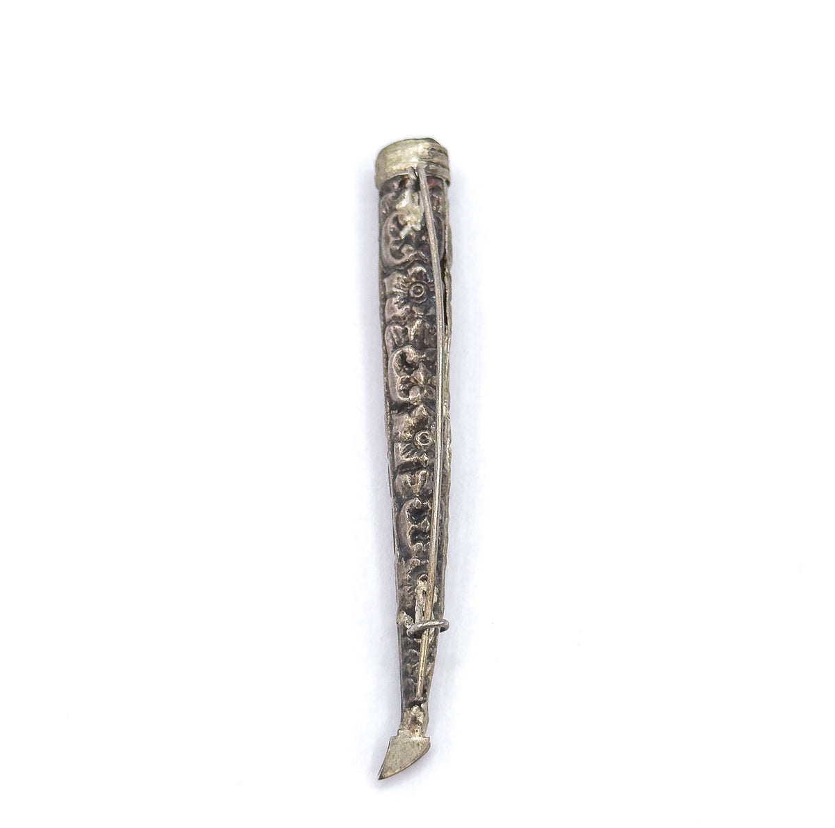 Viewed from the side with the pin stem running the length of the cone and crossing the catch near the tapered tip, the repoussé scrolls and a small flower motif catching light along the body.