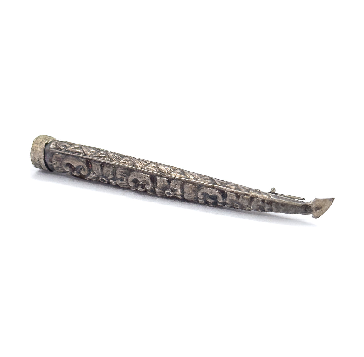 Laid on the diagonal with the collared rim at upper left, a band of small triangles edging the upper side above the scrolled repoussé, the pin stem emerging past the tapered tip at lower right.