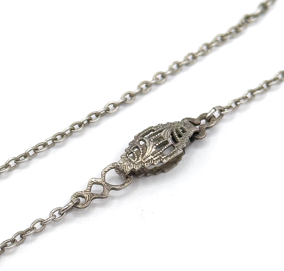 A close crop of the fine cable chain against white, centred on its ornate patterned clasp and the small figure-eight link beside it, showing the darkened patina of the silver.