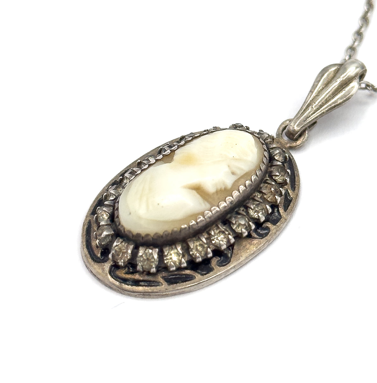 An angled three-quarter view of the pendant, showing the depth of the bezel, the prongs gripping each glass stone, the dark enamel scrolls around the frame and the fluted bail edge-on.