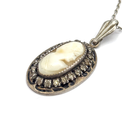 An angled three-quarter view of the pendant, showing the depth of the bezel, the prongs gripping each glass stone, the dark enamel scrolls around the frame and the fluted bail edge-on.