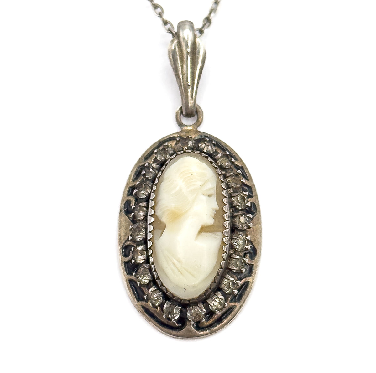 A tight close-up filling the frame with the cameo's carved hair and profile, each prong-set glass stone and the dark enamel scrollwork clearly visible, the fluted bail above.