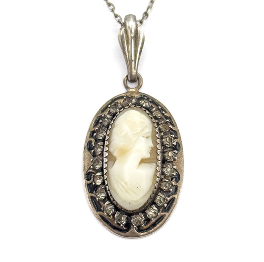 A tight close-up filling the frame with the cameo's carved hair and profile, each prong-set glass stone and the dark enamel scrollwork clearly visible, the fluted bail above.