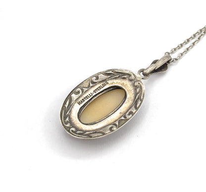 A mid-century sterling silver cameo pendant necklace shown from the back against white, its scrolled oval frame stamped "Martelli Sterling", with bail and chain trailing up to the right.