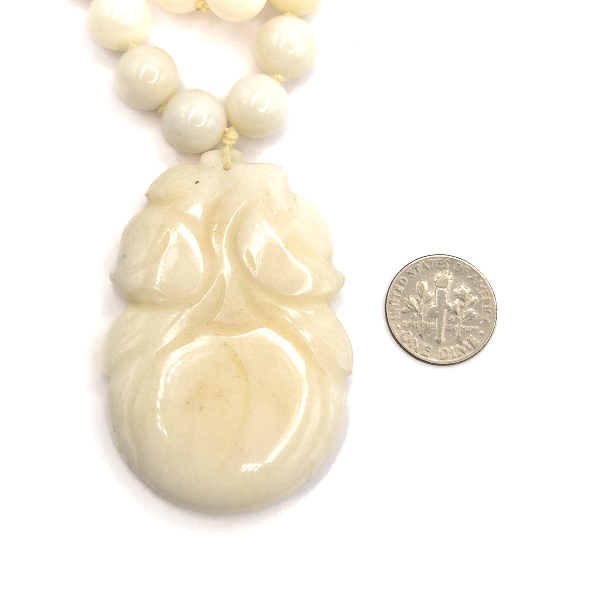 The carved jade gourd pendant lies flat beside a dime for scale, hanging on knotted cord below the strand of round beads.
