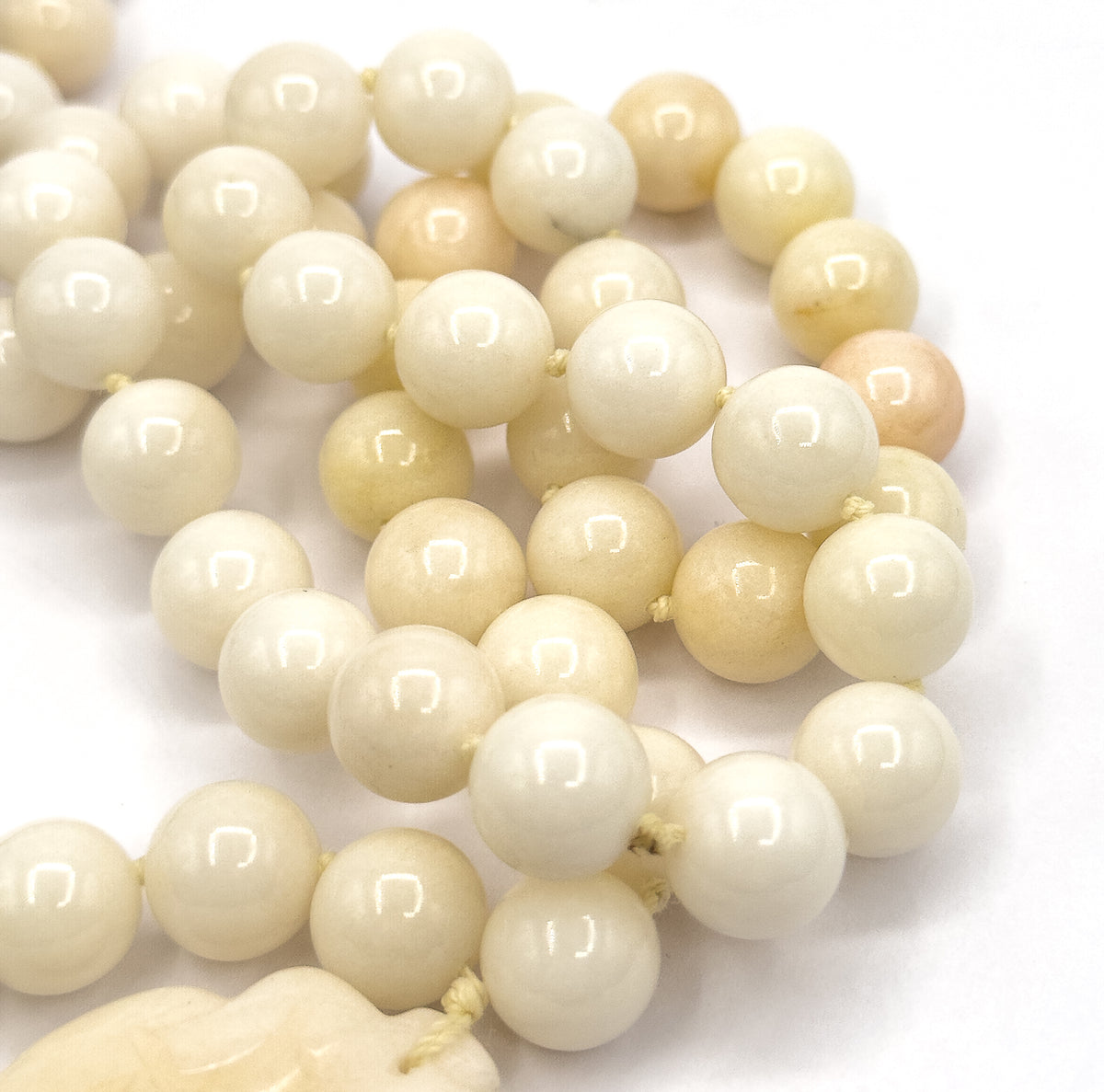 Extreme close-up of the coiled strand filling the frame, each round jade bead showing a bright highlight, with the top edge of the carved pendant just entering the lower corner.