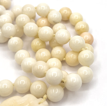 Extreme close-up of the coiled strand filling the frame, each round jade bead showing a bright highlight, with the top edge of the carved pendant just entering the lower corner.