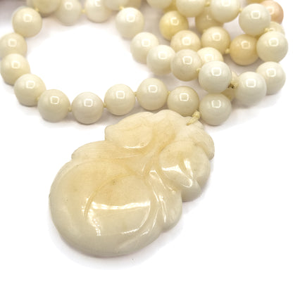 The carved gourd pendant fills the lower frame in sharp detail, its scrolling leaf and fruit forms polished smooth, with the looping strand of beads receding behind it.