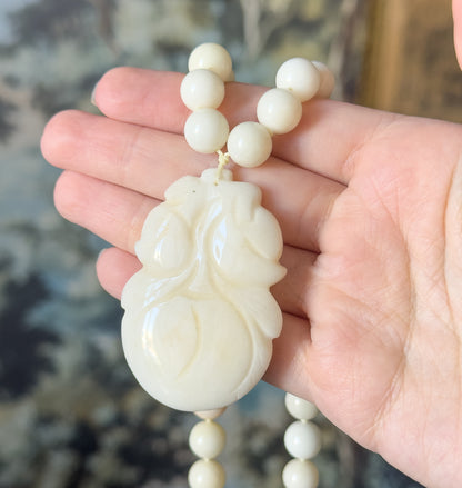 The carved gourd pendant rests across the fingers of an open hand, cord knot visible at its top, with the jade beads looping above and below the palm.