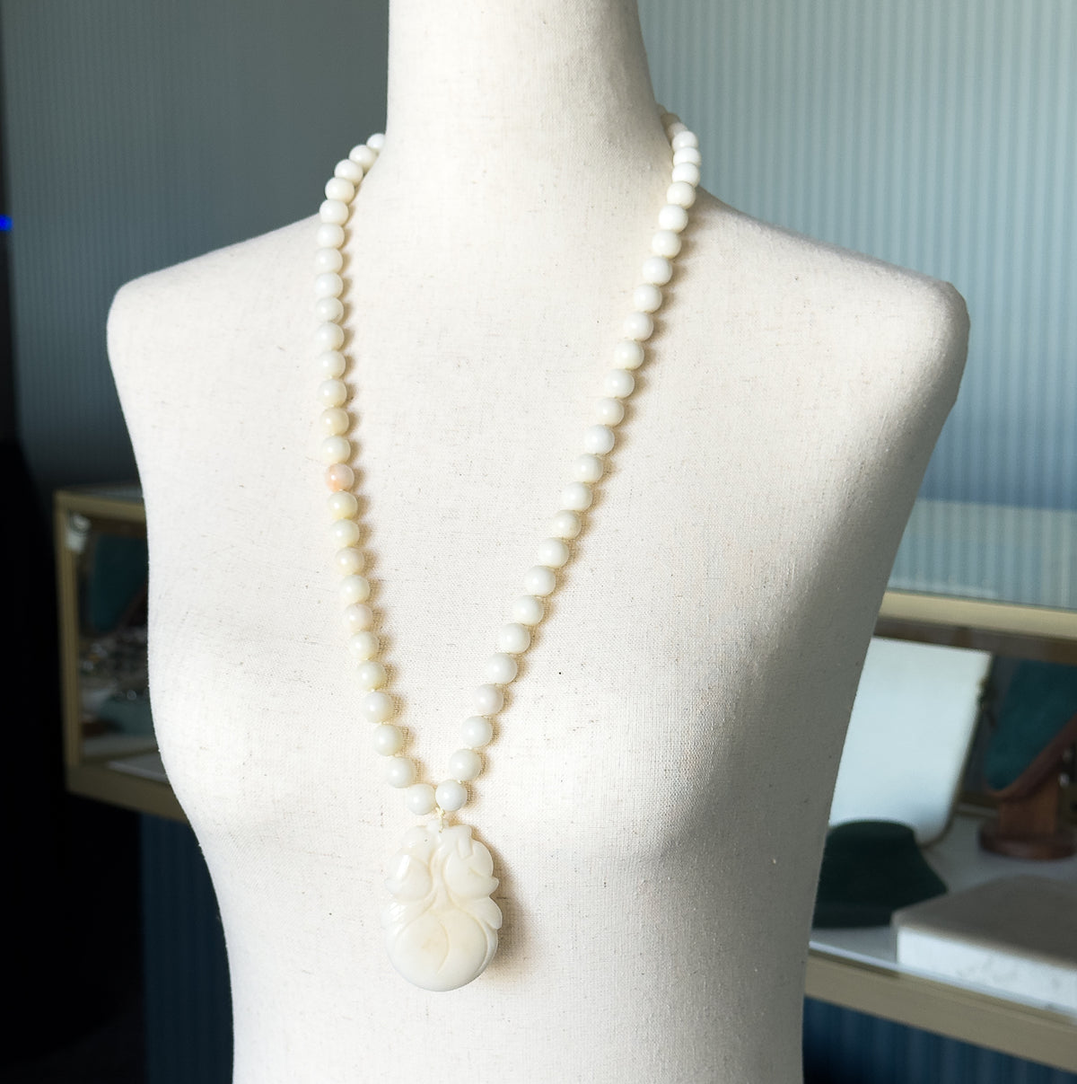 Shown on a pale fabric dress form, the long strand hangs from the neck to well below the bust, the carved gourd pendant swinging free at the lowest point of the loop.