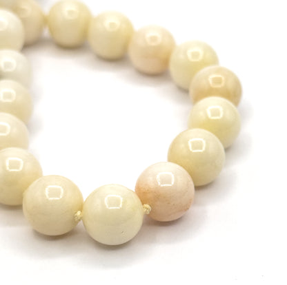Mid-Century carved jade gourd pendant necklace, shown in close-up on white as a curving line of round polished jade beads in creamy white to soft peach, knotted between beads.