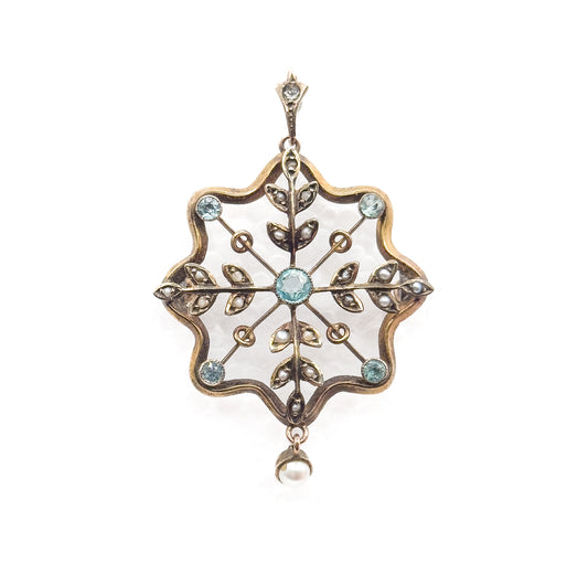 Straight-on upright view showing the whole pendant from the small stone-set bail at top, through the scalloped frame with its blue paste bezels and seed pearl leaves, to the pearl drop below.