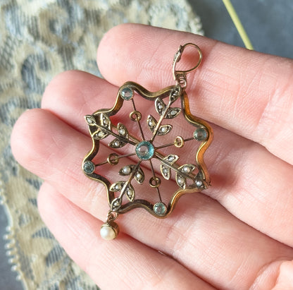 Resting flat across four fingers, the pendant spans most of their width, showing its scale, with the bail at top and the seed pearl drop hanging past the fingertip below.