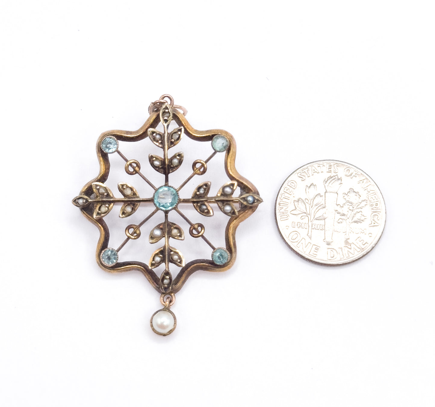 Laid flat beside a dime on white, the pendant stands about twice the coin's width, its scalloped gold frame, blue paste bezels and pearl drop clearly compared.