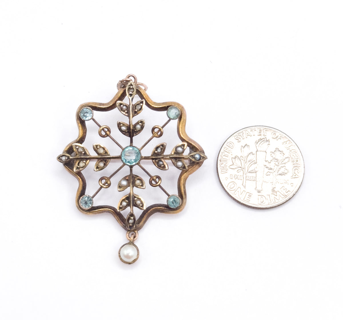 Laid flat beside a dime on white, the pendant stands about twice the coin's width, its scalloped gold frame, blue paste bezels and pearl drop clearly compared.