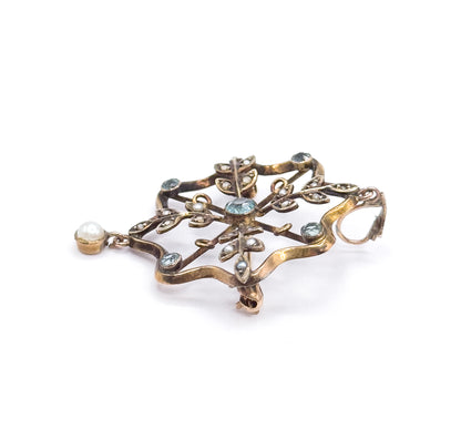 Seen from a low side angle on white, the pendant's bezels and pearl leaves stand up in relief, the bail loop turned to the right and the pearl drop swinging from its cup at the left.