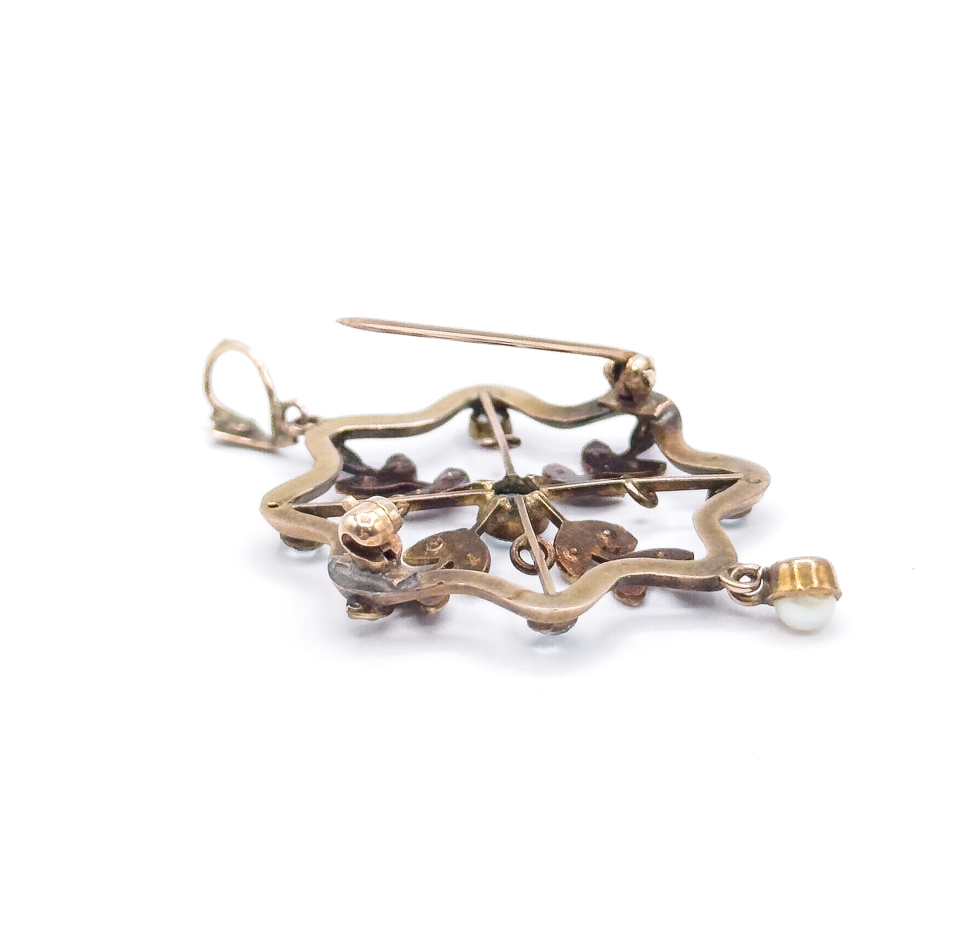 The back of the pendant faces up, showing the long pin stem crossing the open scalloped frame, the bezel backs and pearl settings underneath, bail at the left and pearl drop in its cup at the right.