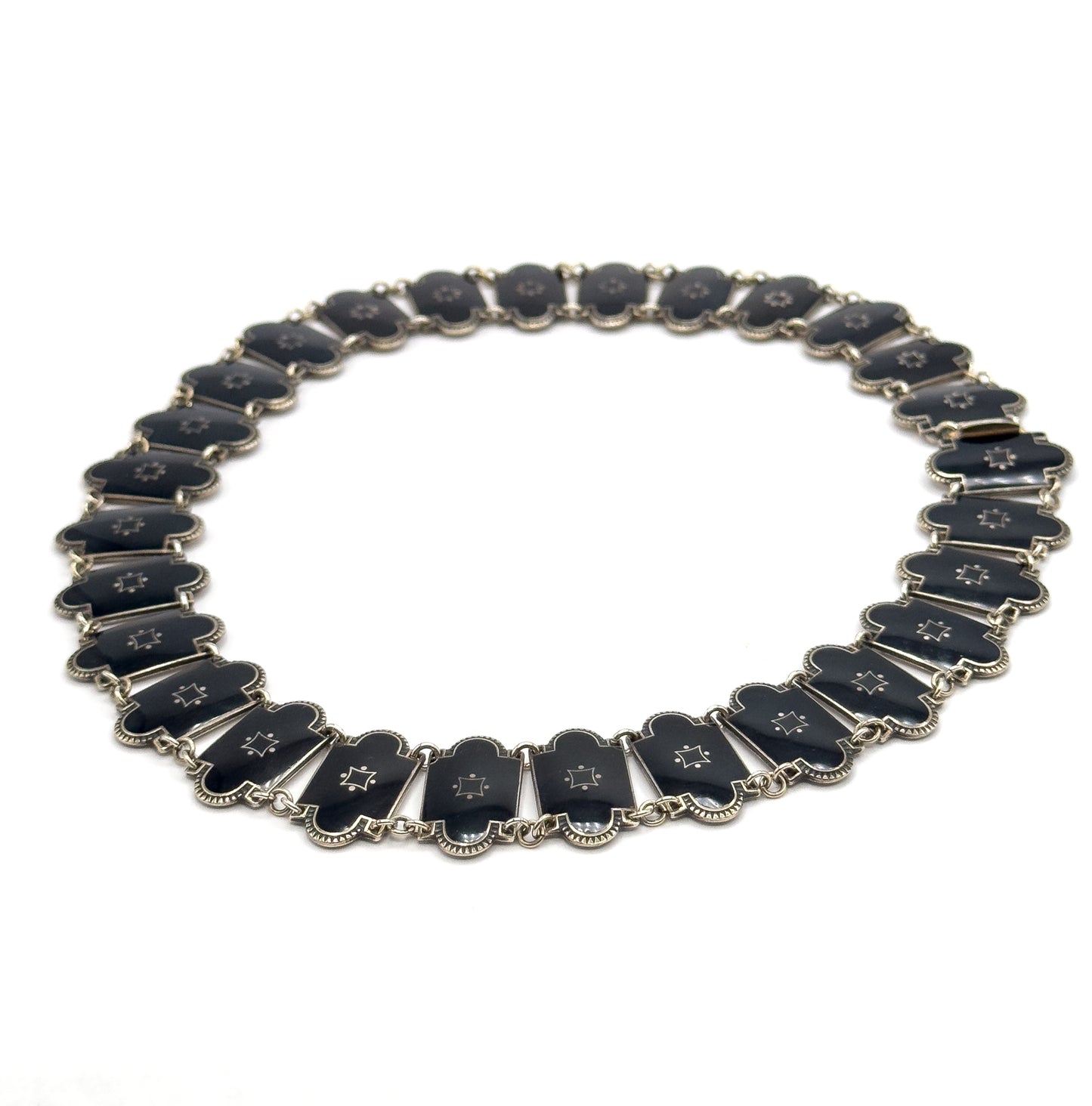 The whole necklace closed into an oval on white, seen at a low tilt so the far links recede and the near ones stand slightly on edge, with the clasp fitting visible at the upper right.