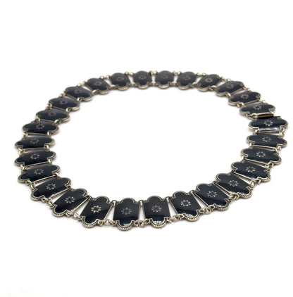 The whole necklace closed into an oval on white, seen at a low tilt so the far links recede and the near ones stand slightly on edge, with the clasp fitting visible at the upper right.
